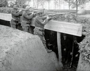 Soldados europeus disparam rifles a partir de uma trincheira enquanto outros permanecem protegidos abaixo, ilustrando o combate estático da Primeira Guerra Mundial.