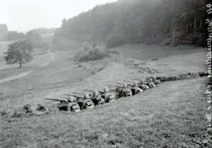 Soldados da Primeira Guerra Mundial posicionados em linha defensiva no campo, armados com rifles, refletindo a transição da guerra de avanço para a guerra de posições