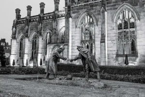 Escultura em Liverpool representa dois soldados da Primeira Guerra Mundial apertando as mãos com uma bola de futebol aos pés, simbolizando a Trégua de Natal de 1914 e seu legado histórico.